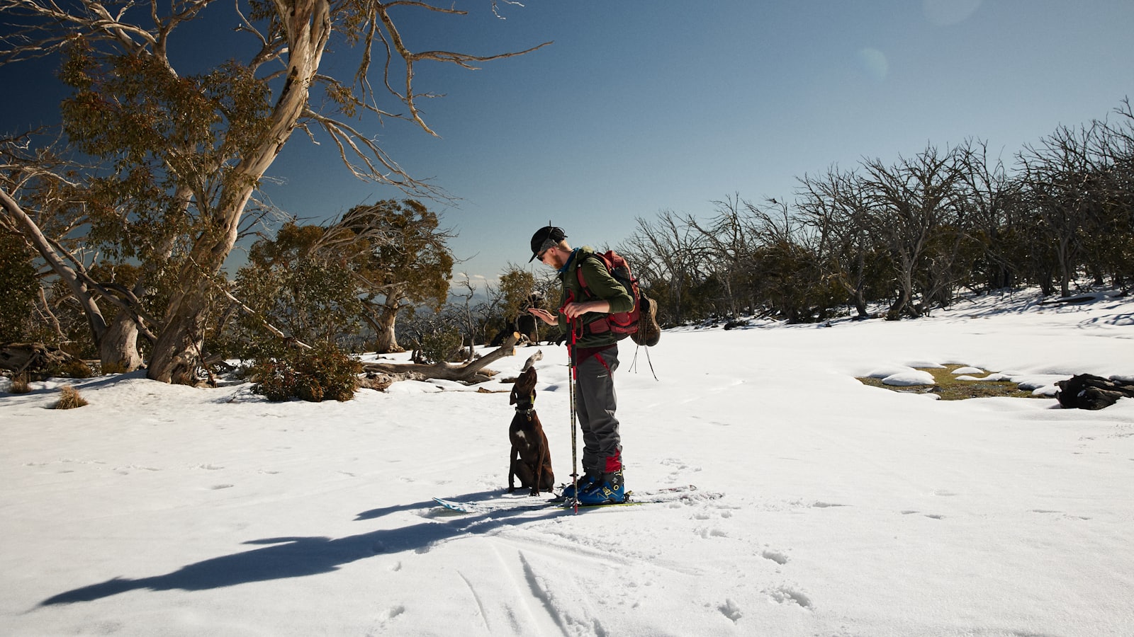 man in red jacket and black pants standing on snow covered ground during daytime