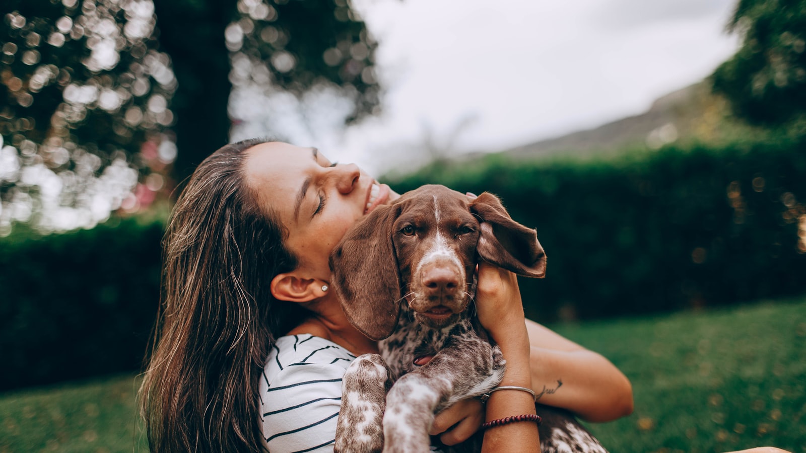 woman in white and black stripe tank top hugging brown and white short coated dog
