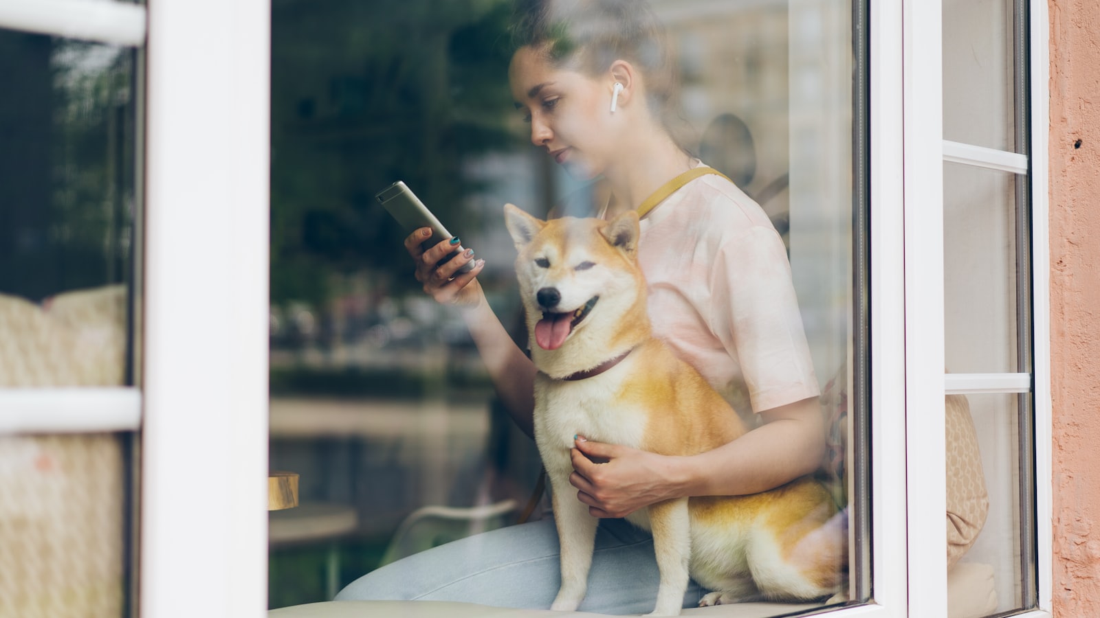a woman sitting on a window sill holding a dog