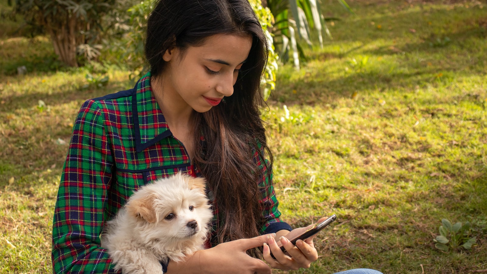 a woman sitting on the ground holding a dog and a cell phone