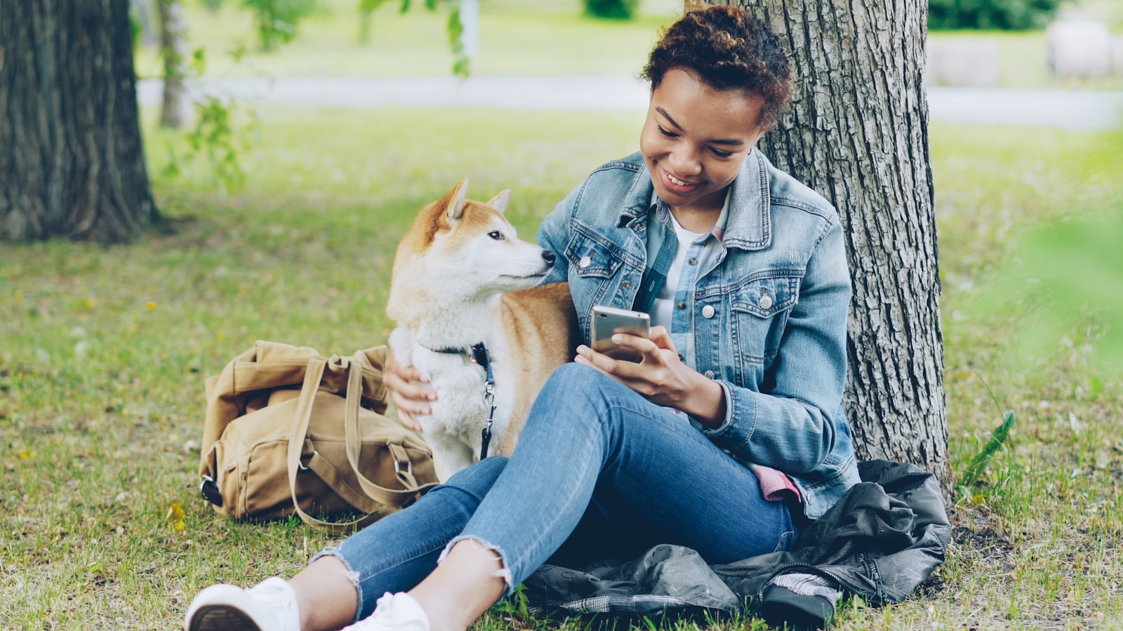 Woman with dog looks at her phone outside.